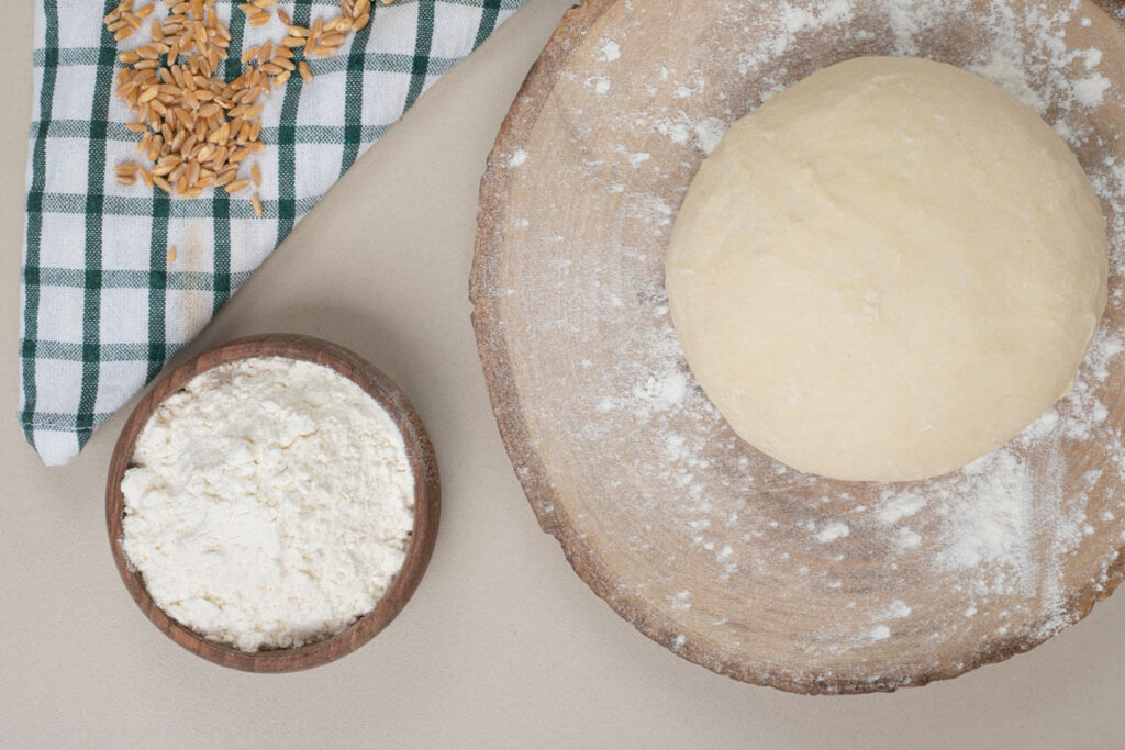 image of wheat flour in a bowl and wheat dough on a wooden board