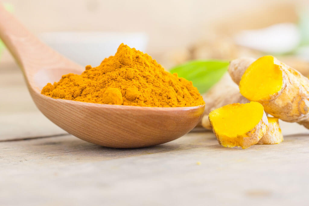 image showing turmeric and turmeric powder in a wooden spoon